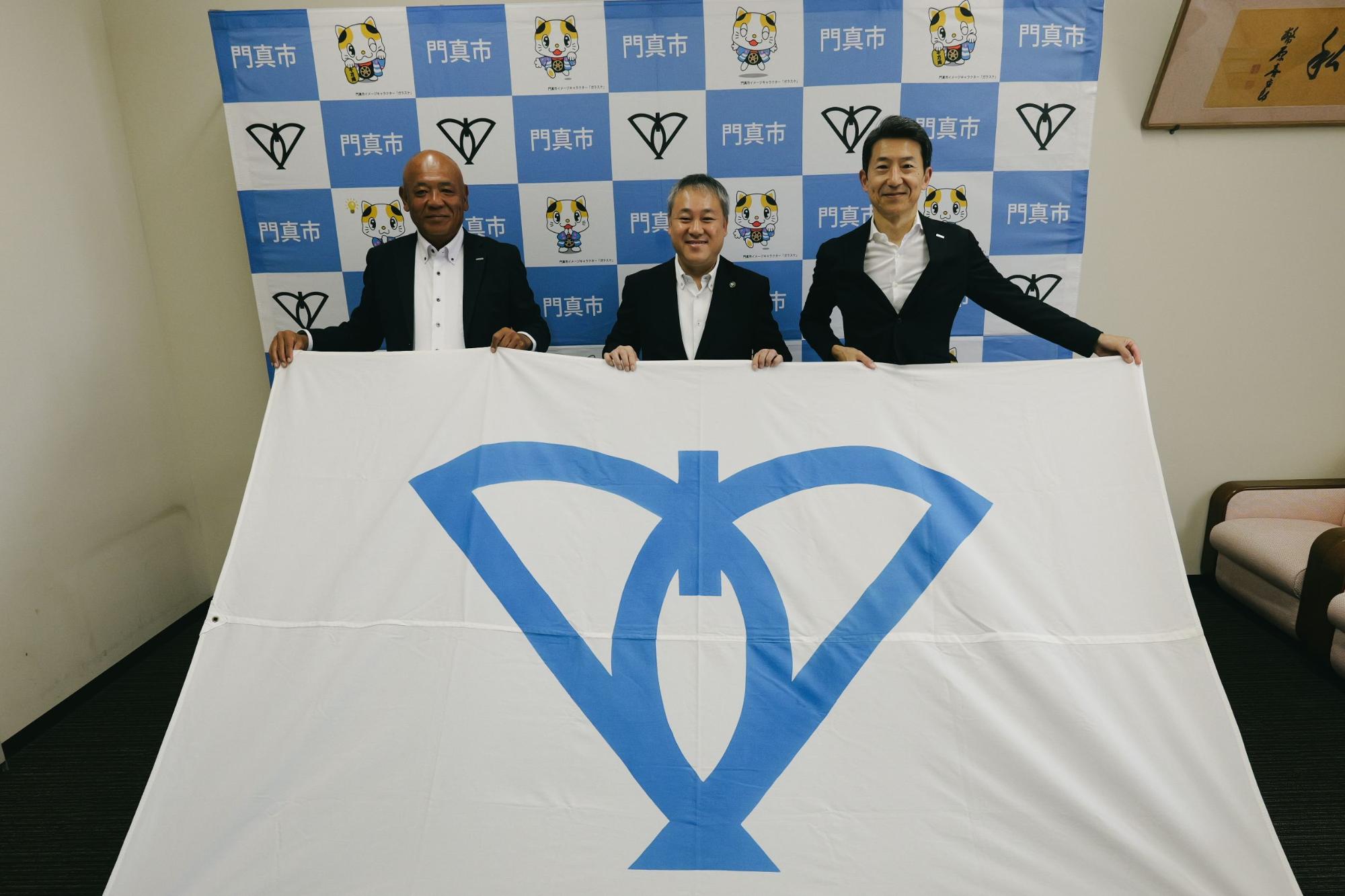 3人で門真市旗を広げて撮った写真です