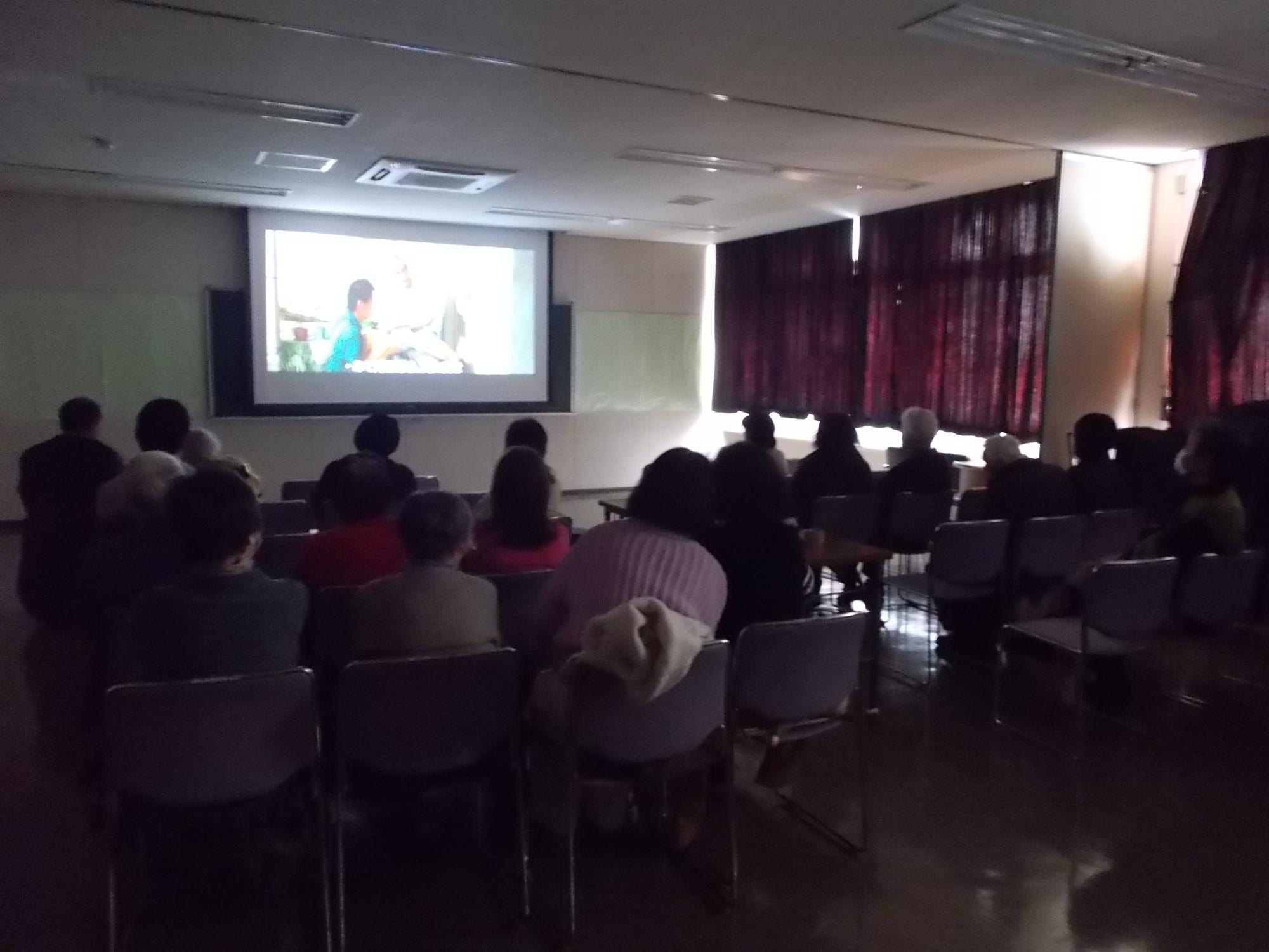 暗い部屋の中央、大きなスクリーンに映し出された映画「海角七号君想う国境の南」を観る人たち
