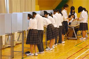 投票用紙を受け取り記載台で記入する生徒の写真